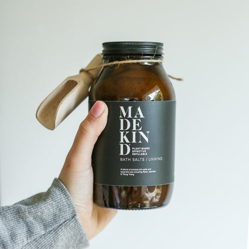 Photo of a hand holding MadeKind bath salts in an amber glass bottle